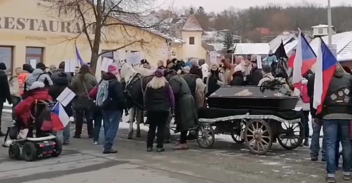 Před Blatného domem protestovaly desítky lidí s vlajkami a transparenty, koně táhli rakev